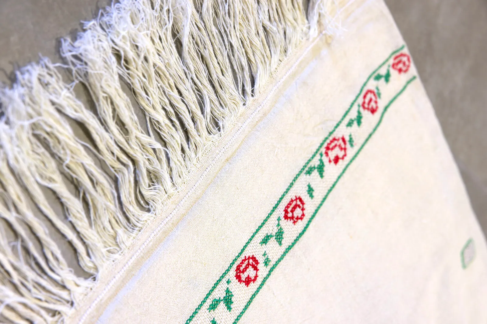 La fascia di rose rosse e foglie verdi ricamata a punto croce, accanto alle frange