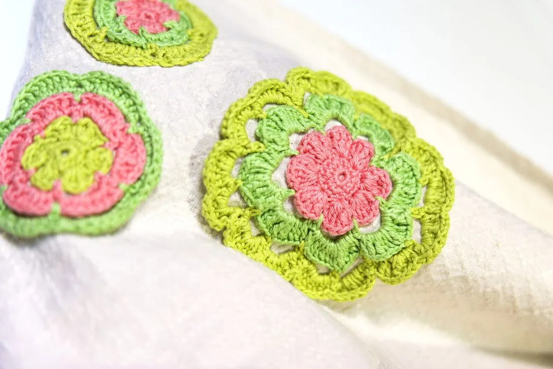 Fiori all'uncinetto rosa, verdi e gialli cuciti su un telo di cotone tessuto a telaio